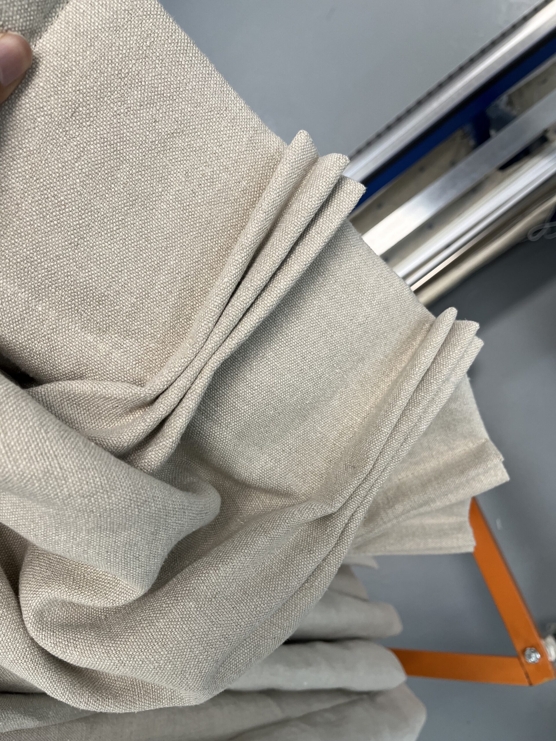 A hand holding a pleated section of linen drapery fabric.