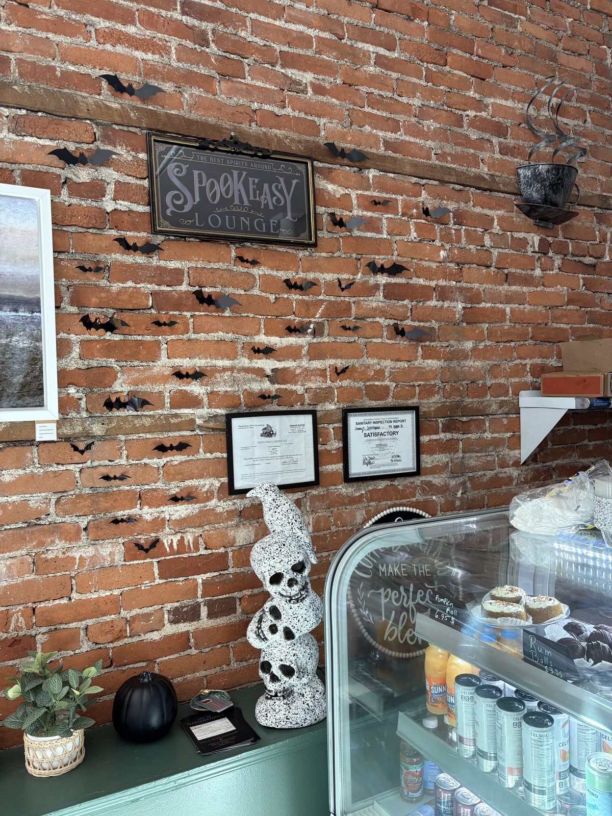 Jimmy's Coffeehouse, Clinton - a brick wall with a Spookeasy Lounge sign, paper bats and a pastry case