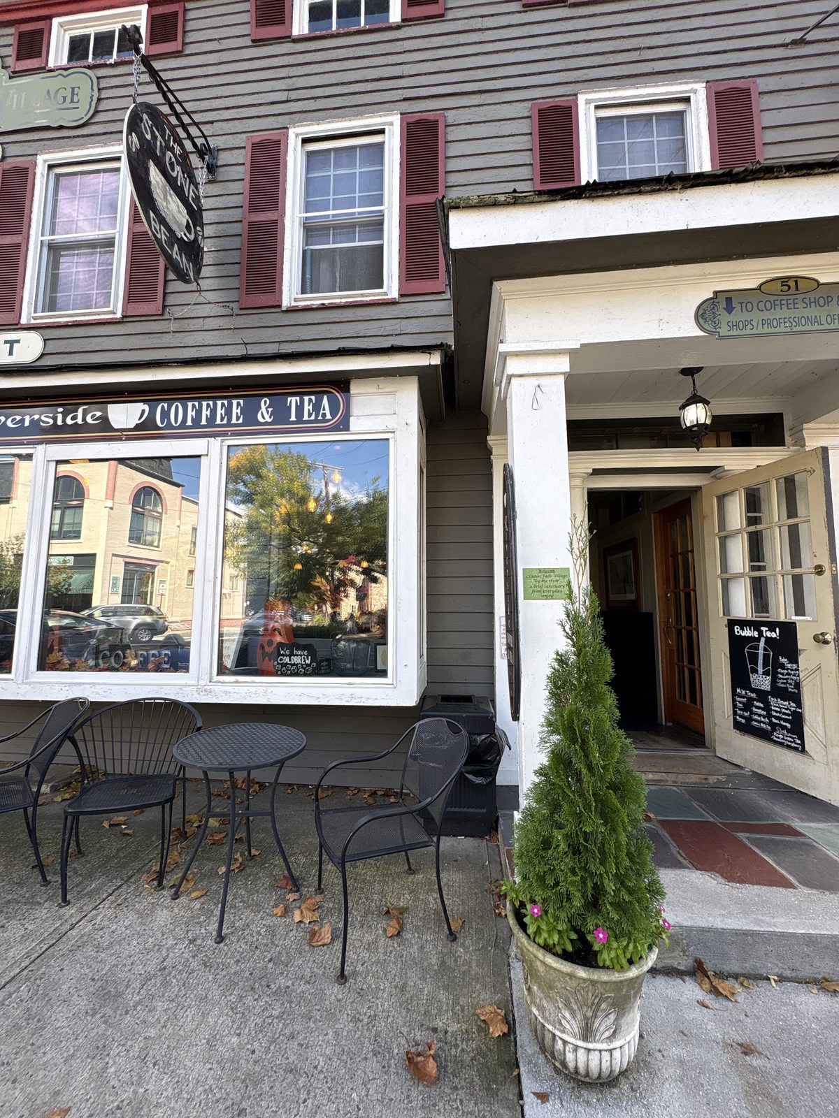 The Stone Bean, Clinton - the storefront at 51 Main Street with a bistro table and chairs on the sidewalk and a hanging Stone Bean sign